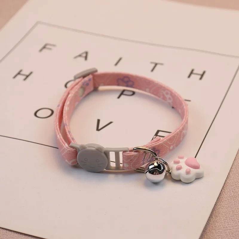 Adjustable cat collar in blue with white paw prints, quick-release buckle, and safety bell.