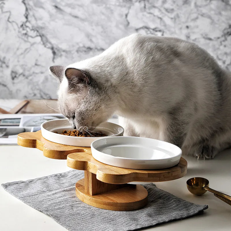 Dual white ceramic cat bowls in elevated natural bamboo stand, perfect for food and water.